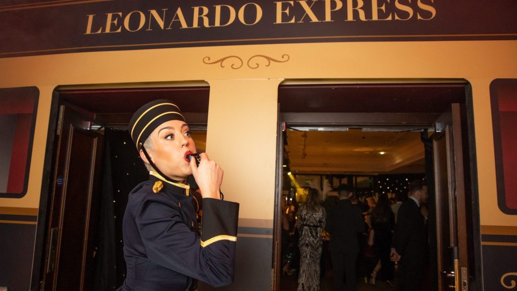 Train conductor blows whistle for train at the Leonardo Hotel's Annual Employee Awards Dinner organised by The Wentworth Collective, Business Events Agency. Sign above train door reads "Leonardo Express"